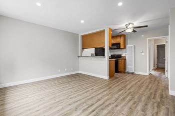 An empty living room with a kitchen and a ceiling fan